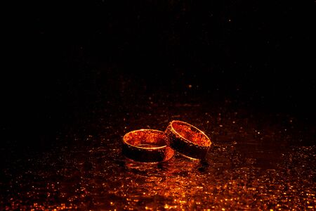 Wedding rings with water drops on a dark orange backlight background.の写真素材