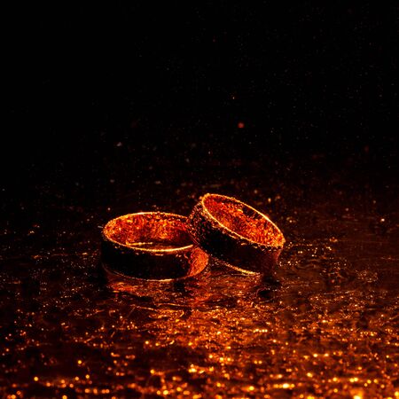 Wedding rings with water drops on a dark orange backlight background.の写真素材