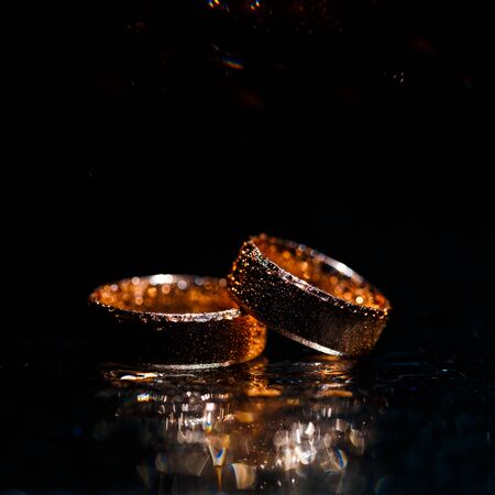 Beautiful wedding golden rings on dark wet glass.の写真素材