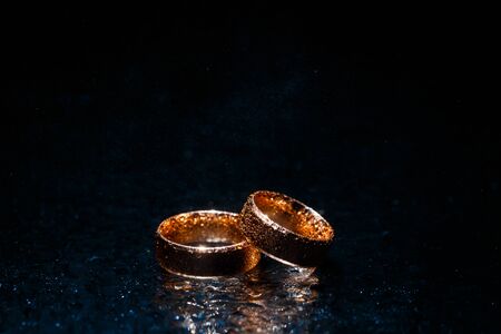 Beautiful wedding golden rings on dark wet glass.の写真素材