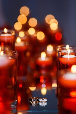 Wedding rings with precious stones on the mirror with many red candles. Beautiful wedding rings with reflection in the mirror.の写真素材