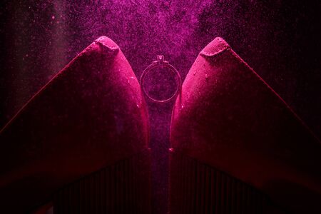 Bride's jewel ring between women's shoes with splashes of perfume in the violet backgroundの写真素材