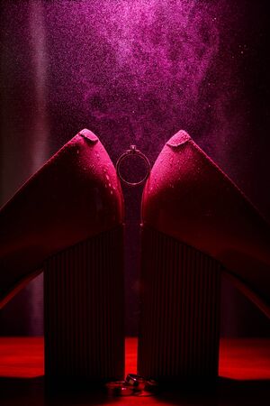 Bride's jewel ring between women's shoes with splashes of perfume in the violet backgroundの写真素材
