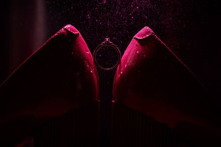 Bride's jewel ring between women's shoes with splashes of perfume in the violet backgroundの写真素材