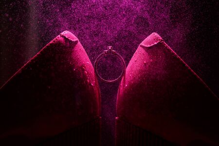 Bride's jewel ring between women's shoes with splashes of perfume in the violet backgroundの写真素材