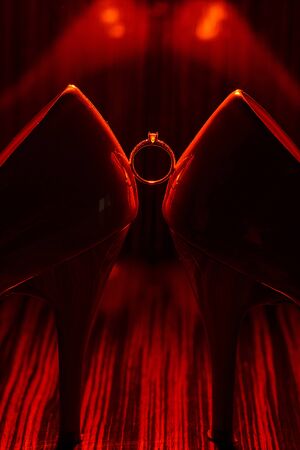 Bride's jewel ring between women's shoes with orange splashes of perfume in the orange background. Wedding concept with ring.の写真素材