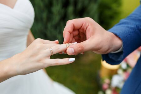 Hands of wedding couple putting golden rings to finger of each other during the ceremony. Newlyweds with rings on the ceremony.の写真素材
