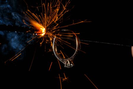 Wedding engagement ring on burning bengal light with many sparks and water spray on dark background. Marriage proposal for Christmas.の写真素材