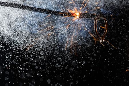 Wedding engagement ring on burning bengal light with many sparks and water spray on dark background. Marriage proposal for Christmas.の写真素材