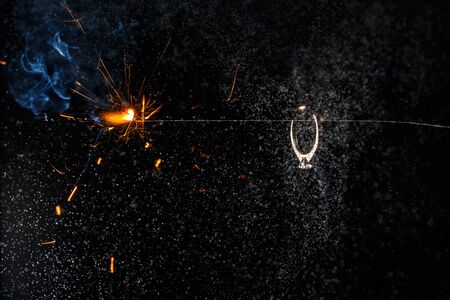 Wedding engagement ring on burning bengal light with many sparks and water spray on dark background. Marriage proposal for Christmas.の写真素材