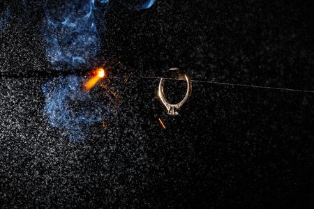 Wedding engagement ring on burning bengal light with many sparks and water spray on dark background. Marriage proposal for Christmas.の写真素材