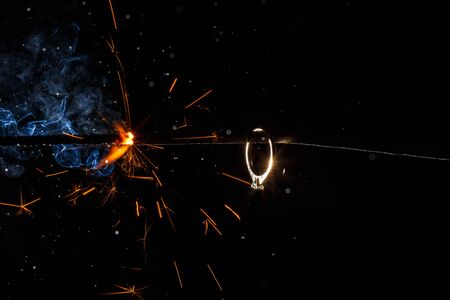 Wedding engagement ring on burning bengal light with many sparks and water spray on dark background. Marriage proposal for Christmas.の写真素材