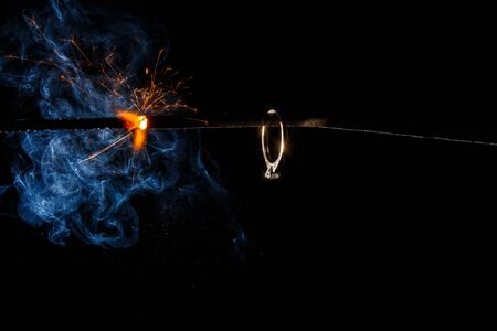 Wedding engagement ring on burning bengal light with many sparks and water spray on dark background. Marriage proposal for Christmas.の写真素材