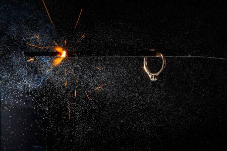 Wedding engagement ring on burning bengal light with many sparks and water spray on dark background. Marriage proposal for Christmas.の写真素材