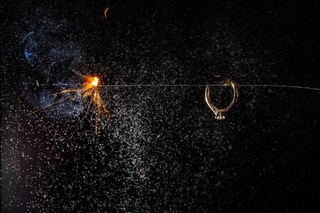 Wedding engagement ring on burning bengal light with many sparks and water spray on dark background. Marriage proposal for Christmas.の写真素材