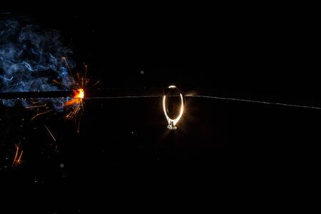 Wedding engagement ring on burning bengal light with many sparks and water spray on dark background. Marriage proposal for Christmas.の写真素材