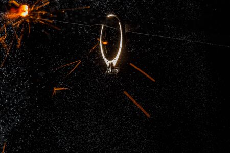 Wedding engagement ring on burning bengal light with many sparks and water spray on dark background. Marriage proposal for Christmas.の写真素材