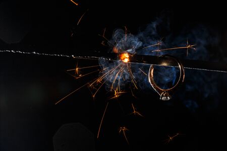 Wedding engagement ring on burning bengal light with many sparks and water spray on dark background. Marriage proposal for Christmas.の写真素材