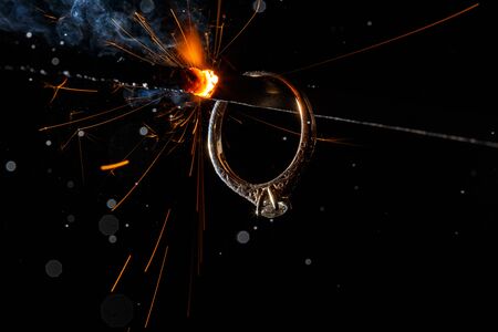 Wedding engagement ring on burning bengal light with many sparks and water spray on dark background. Marriage proposal for Christmas.の写真素材