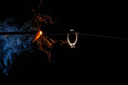 Wedding engagement ring on burning bengal light with many sparks and water spray on dark background. Marriage proposal for Christmas.の写真素材