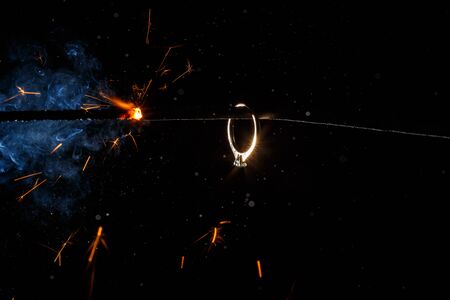 Wedding engagement ring on burning bengal light with many sparks and water spray on dark background. Marriage proposal for Christmas.の写真素材