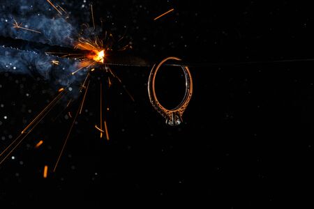 Wedding engagement ring on burning bengal light with many sparks and water spray on dark background. Marriage proposal for Christmas.の写真素材