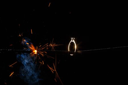 Wedding engagement ring on burning bengal light with smoke and many sparks on dark background. Marriage proposal for Christmas.の写真素材