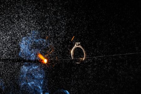 Wedding engagement ring on burning bengal light with smoke and many sparks on dark background. Marriage proposal for Christmas.の写真素材