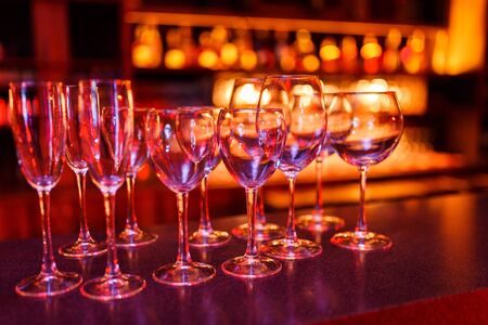 Glasses of wine and champagne stand on the bar in the light of the lights of the night bar