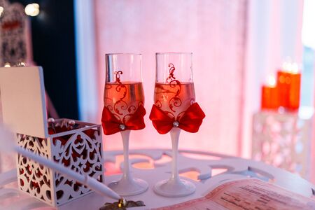 wedding glasses with champagne decorated with a red bow on the table for the bride and groom at the engagement ceremonyの写真素材