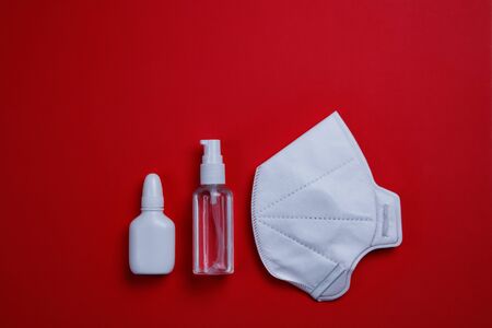 White protective mask, sanitizer and nasal drops on a red background.の写真素材