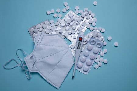 Pills and white medical mask. Protective face mask, thermometer on blue background, against Novel coronavirus 2019-nCoV or Wuhan coronavirus . Copy space.の写真素材
