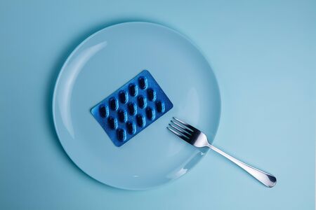 Pills on plate with fork and knife on blue background.の写真素材