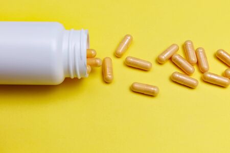 Orange pills capsules scattered from a white jar on a yellow background.の写真素材