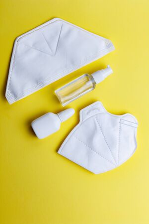 Two types of protective face masks and hand sanitizer on yellow background. Protective masks as precaution in spread of coronavirus 2019-nCoV, flat lay.の写真素材