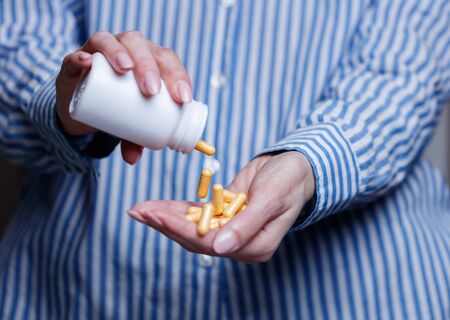 Pills are poured into female doctor hand from a jar, pills in hand, orange vitamins, jar with tablets, close-up.の写真素材