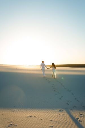 Newlyweds walk barefoot on the sand in the white desert at sunset.の写真素材