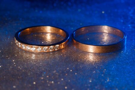 A pair of gold wedding rings with blue neon bokeh background with smoke.