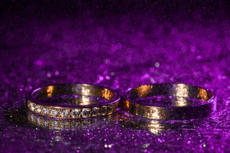 Wedding rings with water drops on a dark violet neon backlight background.の写真素材