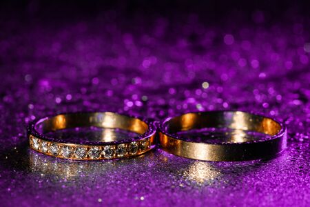 Wedding rings with water drops on a dark violet neon backlight background.の写真素材