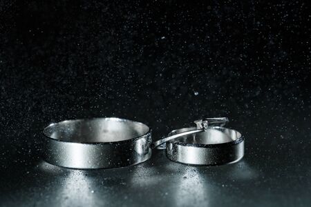Beautiful wedding silver rings on dark wet glass with water drops.の写真素材