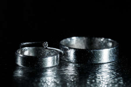 Beautiful wedding silver rings on dark wet glass with water drops.の写真素材