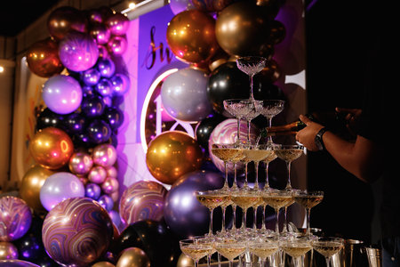 Waiter pours champagne on a slide of glasses. Champagne pyramid for parties at Birthday, party in restaurant. Glasses with champagne in the form of a slide. 2021の写真素材