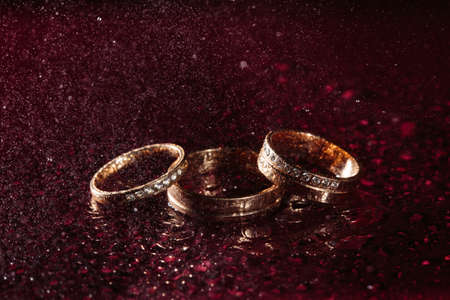Wedding rings on dark water surface shining with light. Rain, water dropsの写真素材