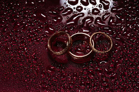 Wedding rings on dark water surface shining with light. Rain, water dropsの写真素材