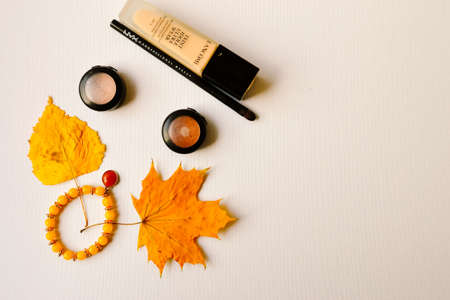 Hove, UK, 03/11/2019. Description: Flat layout of foundation by 'Lancome' company, 'Accessorize' bracelet, yellow earrings, shadows and eyeliner from Nyx, and yellow dry leaves.のeditorial素材