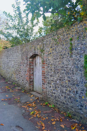 Old stone wall with a wooden door in the middle of the streetの写真素材
