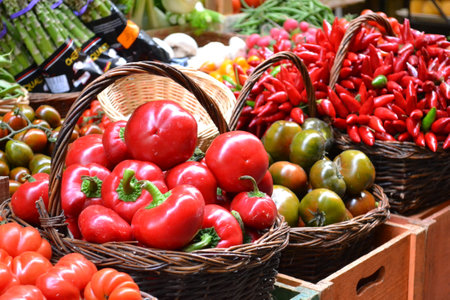 Fresh red bell peppers and other vegetables in baskets on a market stallの写真素材