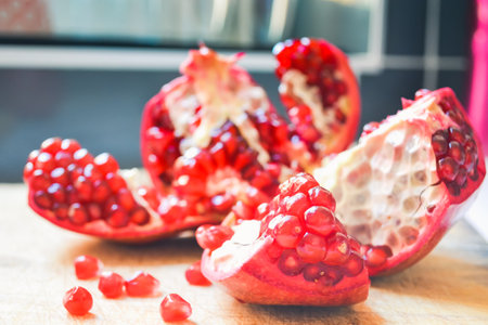 Red pomegranate torn into several pieces with berries falling nearbyの写真素材