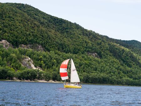 Sailing yacht on river, regatta on water with forest and mountain on backgroundの写真素材